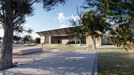 Modern building with wide overhanging roof, landscaped entry path, and trees in the foreground.