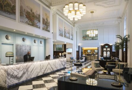 Luxurious heritage hotel lobby with marble reception desk, ornate ceiling, and modern furnishings.