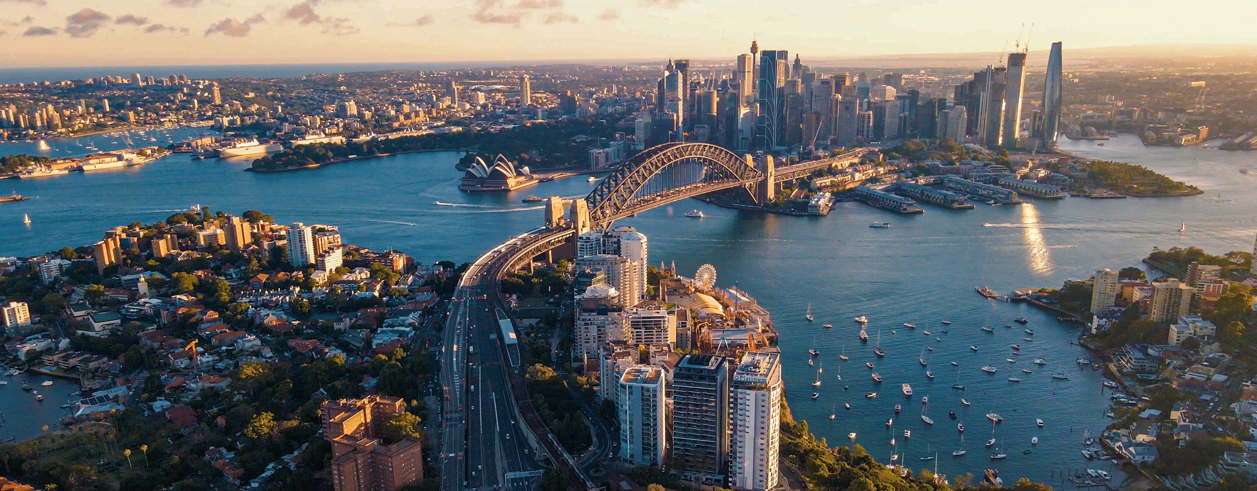 Aerial view of Sydney Harbour at sunset, showing the Harbour Bridge, Opera House, CBD skyline and surrounding suburbs from the north shore.
